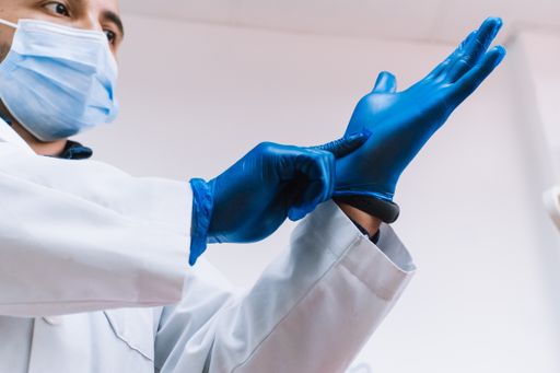 A Hispanic adult male doctor with mask putting on blue latex gloves