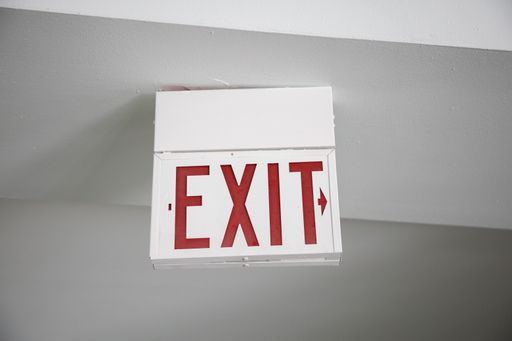 A red and white Exit sign hanging from the ceiling under the lights