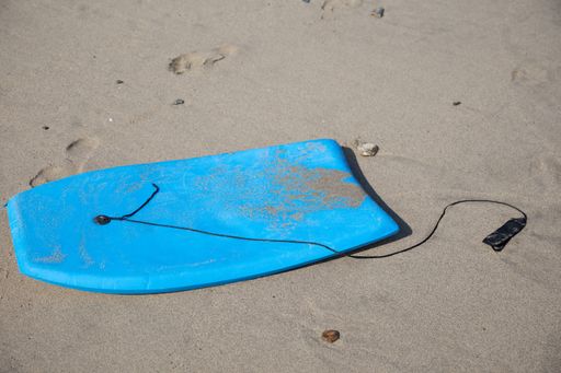 A closeup of a blue bodyboard on the sand in a beach under the sunlight