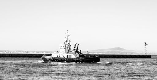Cape Town, South Africa - October 13, 2019: Small Tugboat moving out of safety of harbor in commercial port of Cape Town