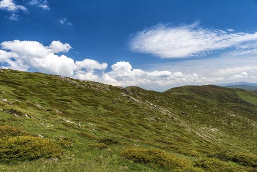 A landscape of hills covered in greenery under the sunlight and a cloudy sky