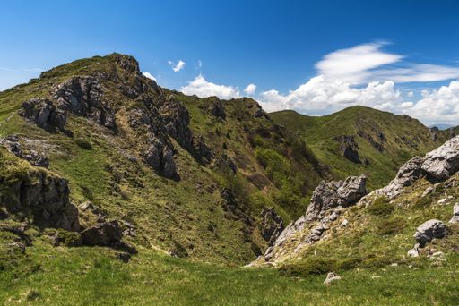 A landscape of rocks covered in greenery under the sunlight and a cloudy sky at daytime