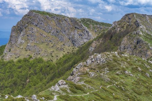A landscape of rocks covered in greenery under the sunlight and a cloudy sky at daytime