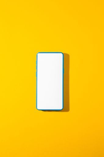 A vertical shot of a blue smartphone with a blank screen on a yellow background