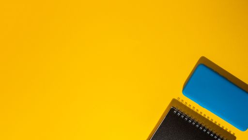 A top view of a smartphone and a notepad on a yellow background