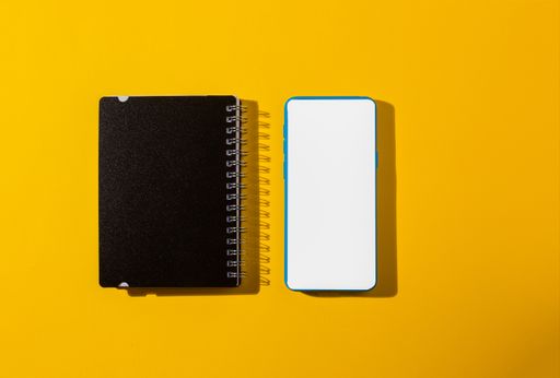A top view of a smartphone and a notepad on a yellow background
