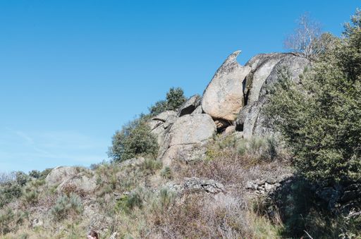 A low angle shot of boulders and bushes on a mountain against a clear blue sky