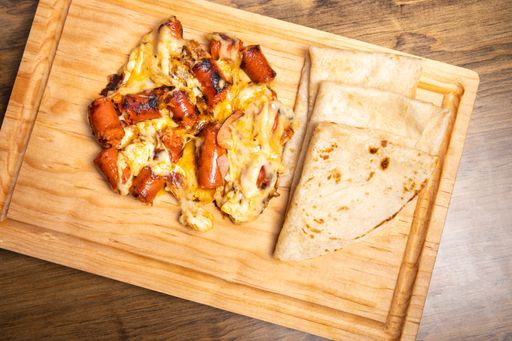 The top view of tortilla and chistorra sausages with melted cheese on wooden cutting board