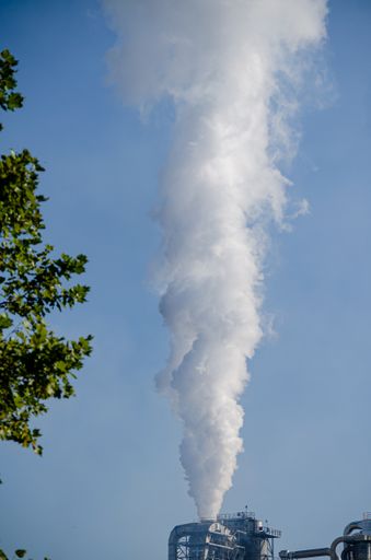 Plume of steam rising from industrial chimney into a blue sky
