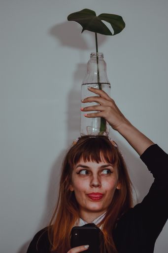 A vertical shot of a funny caucasian female holding a glass bottle with a green leaf on her head