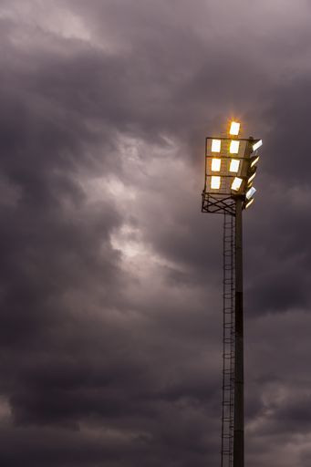 A low-angle shot of bright sports stadium lights against the cloudy sky