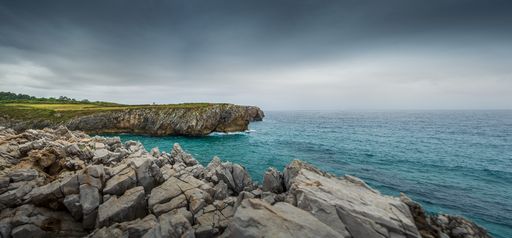 A stunning view of a rocky coastline and vast ocean surrounded by dramatic clouds in Asturias, Spain