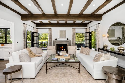 A modern living room with two white couches positioned in front of a fireplace and large windows