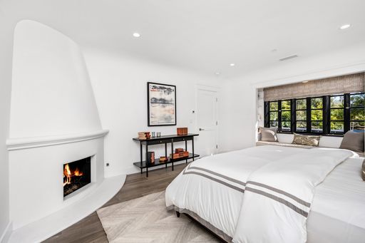 A spacious bedroom features white walls, wood floors, and large windows, creating a bright and inviting atmosphere