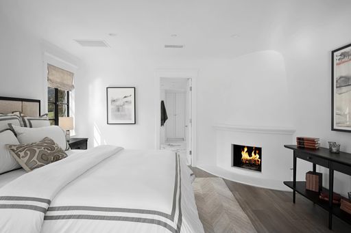 A sophisticated and stylish bedroom with a stunning white color palette and central fireplace as a focal point, creating a luxurious atmosphere