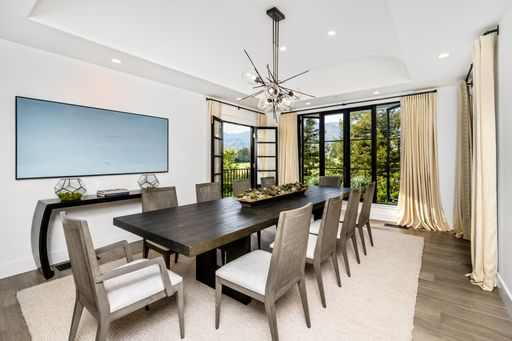 A contemporary white dining room with a sleek table in the center, surrounded by four modern chairs, illuminated by natural light