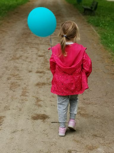 A vertical shot of a little girl with a blue balloon walking on a park