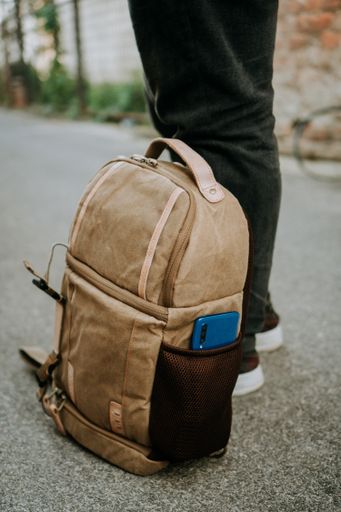 A brown canvas camera bag with a smart phone in the side pocket, on the ground beside the photographer's feet