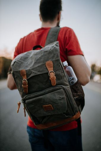 A selective focus shot man standing on the road with a flap backpack and water bottle. Travel concept
