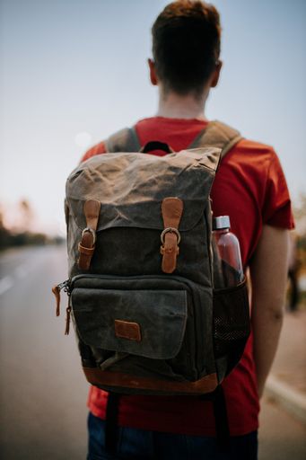 A selective focus shot man standing on the road with a flap backpack and water bottle. Travel concept