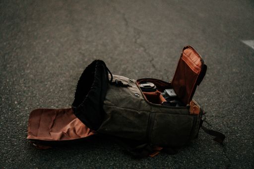 A fully open gray canvas camera utility backpack laid on the ground with cameras and lenses inside