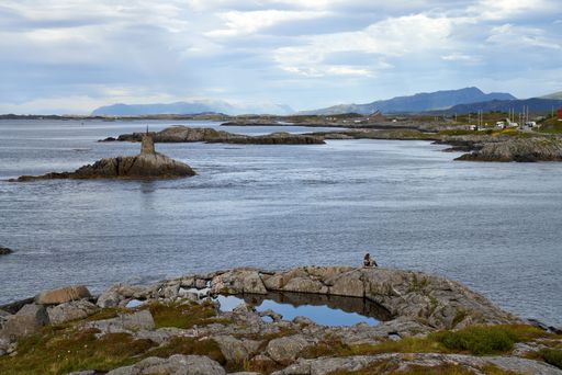A rocky coastline and a lighthouse close to the Atlantic Ocean Road in Norway under a cloudy sky