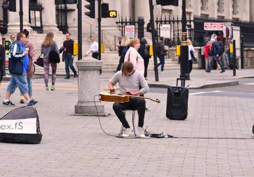 A young adult male performing an acoustic guitar solo on a city sidewalk