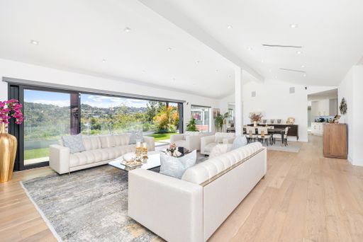 This modern living room with wood floors and high ceilings boasts a large window providing a stunning view of the outside world