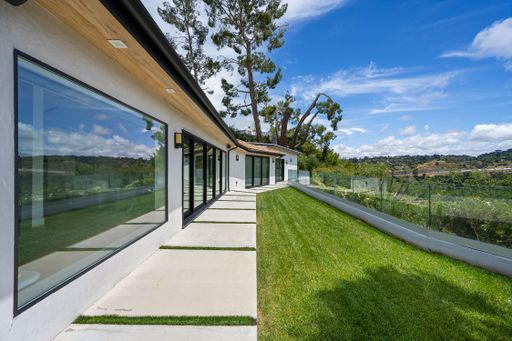 A spacious, grassy backyard with a porch, providing a scenic view of the rolling hills of a vineyard and the distant mountains