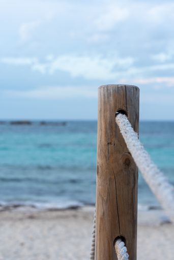 A wooden post on the beach in the background of the sea and clouds in Balearic Islands, Spain