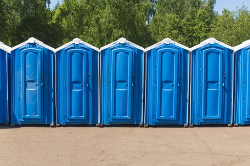Plastic bio public toilet stalls stand in a row against the backdrop of green trees in crowded places