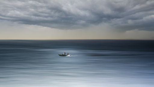 A sailboat is pictured in the open ocean, with a backdrop of dark, ominous clouds