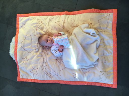 A vertical shot of a baby lying on white sheets decorated with stars and clouds