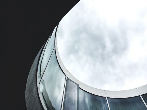 A low angle shot of the inside of a round building in a glass facade with a cloudy sky in the background