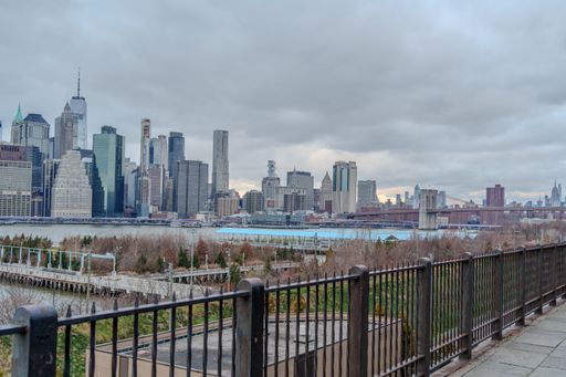 This stock photo features a breathtaking view of the iconic Statue of Liberty surrounded by the sparkling waters of the New York Harbor, with the stunning Manhattan skyline in the background