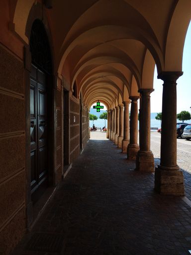 A vertical shot of a sidewalk with concrete columns and a green pharmacy sign hanging
