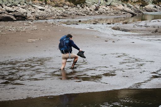A guy with shorts going through a steep muddy lake while holding his boots in his hand