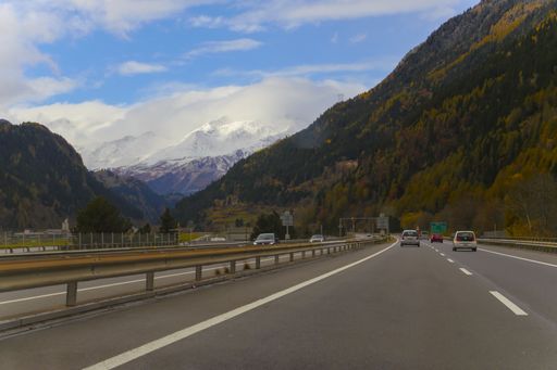 A road surrounded by hills and rocks covered in greenery and snow under a cloudy sky