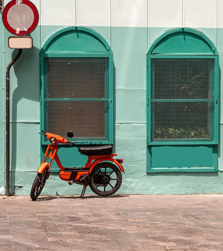 Orange retro motorcycle parked beside a turquoise blue wall with dops windows