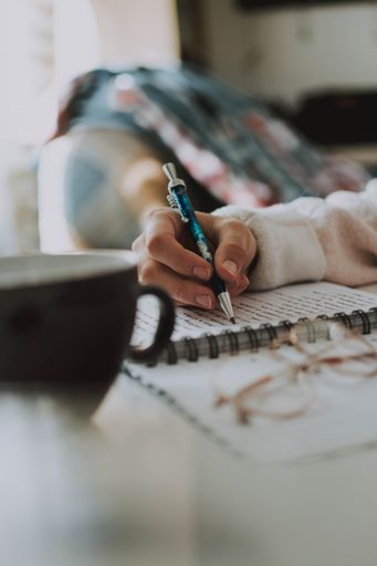 A vertical shot of a female writing something in her notebook with a pen