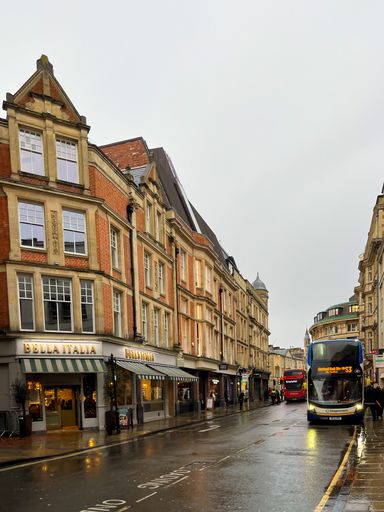 A public bus is parked at the curb in an urban environment during the dusk hours of a rainy day