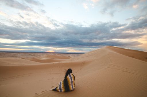 A beautiful wide shot of a female with a cloak sitting on erg desert sand