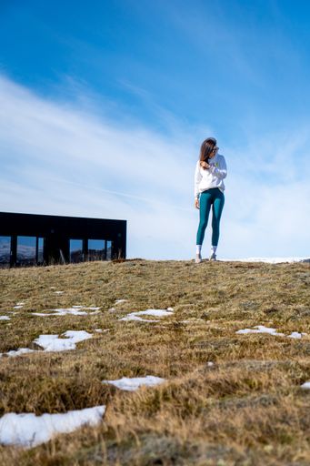 A vertical of a young Caucasian woman standing on a hill against a modern house