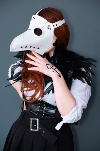 A female cosplayer dressed as a plague doctor with a white mask.