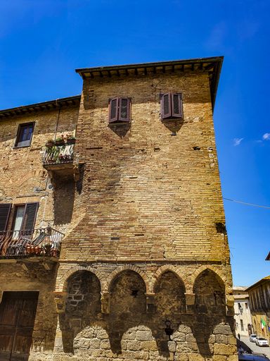 A vertical shot of an old brick building with a balcony under a blue sky in San Gimignano, Italy