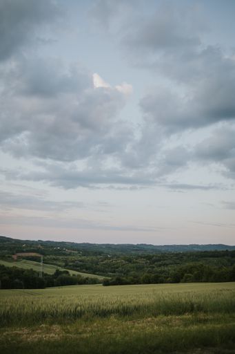 A vertical shot of a cloudy sky above a beautiful landscape with forests, hills and fields