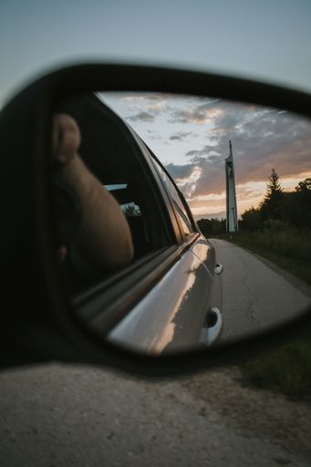 A vertical shot of a tall structure on a road, viewed through the side mirror of a car during sunset