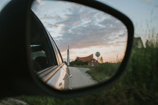 The sunset sky over the village seen in the side-view mirror of a car