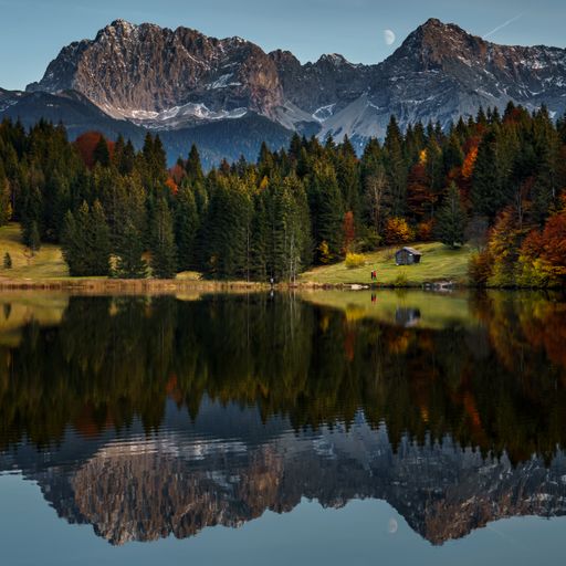 A tranquil landscape with a pristine lake surrounded by majestic mountains, and lush trees lining the shoreline