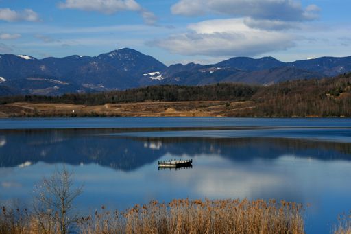 A lake surrounded by hills covered in greenery and reflecting on the water under the sunlight